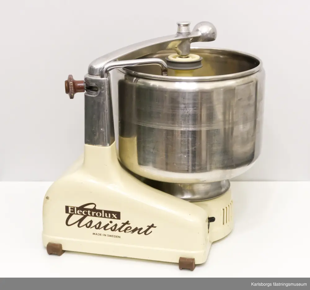 Electrolux assistent, köksmaskin som förmodligen kommer från 1960-talet. Assistentens bas är uppdelad i flera delar: motorstativ med fjädrande arm, ratt, drivuttag för kittel och drivuttag för mixer. Tillbehör: kabel, kittel, rulle, kniv för kittel, skrapa, kvarnhus, kvarnvals, kvarnring, matarskål, matarpropp, kvarnkniv, fin hålskiva, grov hålskiva, rivvals, stänkskydd, matarskruv, korvpipa, passervals, passerventil, passercylinder, passerränna, skyddshatt för drivuttag. Tre tillbehör från settet har blivit borttappade: lockskål, rivcylinder samt passerfjäder. Ihop med köksassistenten kommer en liten bok med innehåll av vilka delar som medföljer maskinen, hur maskinen används och hundra recept. Assistenten är gjord i Sverige.
