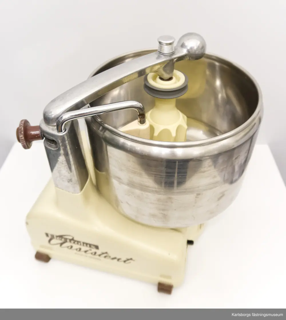 Electrolux assistent, köksmaskin som förmodligen kommer från 1960-talet. Assistentens bas är uppdelad i flera delar: motorstativ med fjädrande arm, ratt, drivuttag för kittel och drivuttag för mixer. Tillbehör: kabel, kittel, rulle, kniv för kittel, skrapa, kvarnhus, kvarnvals, kvarnring, matarskål, matarpropp, kvarnkniv, fin hålskiva, grov hålskiva, rivvals, stänkskydd, matarskruv, korvpipa, passervals, passerventil, passercylinder, passerränna, skyddshatt för drivuttag. Tre tillbehör från settet har blivit borttappade: lockskål, rivcylinder samt passerfjäder. Ihop med köksassistenten kommer en liten bok med innehåll av vilka delar som medföljer maskinen, hur maskinen används och hundra recept. Assistenten är gjord i Sverige.