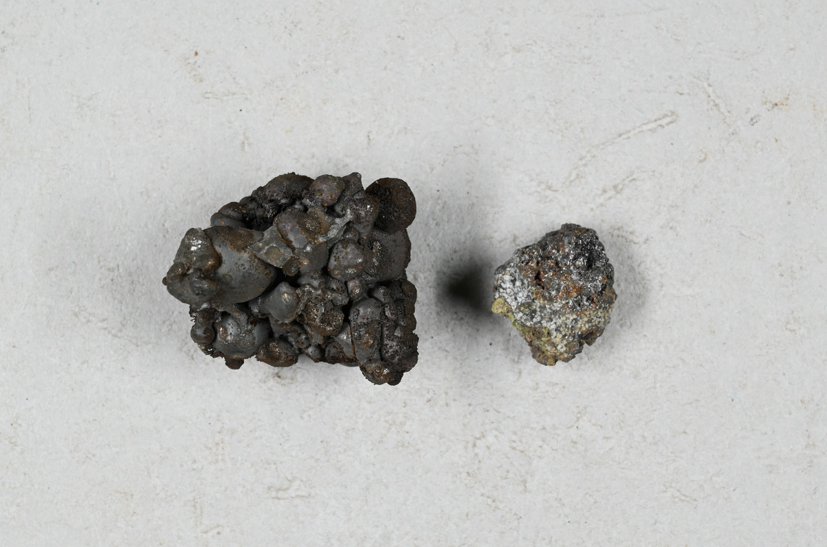 Materialprov, Grå, blå och brunaktig. Tillhörande lapp med notering: "1833 i Mars Garpenberg. Owanligt nas som nu utan ugn bränd ansatt hastigt bildar sig i suluhyttan. Analys as Schiälberg (?) d. 28/8 33."