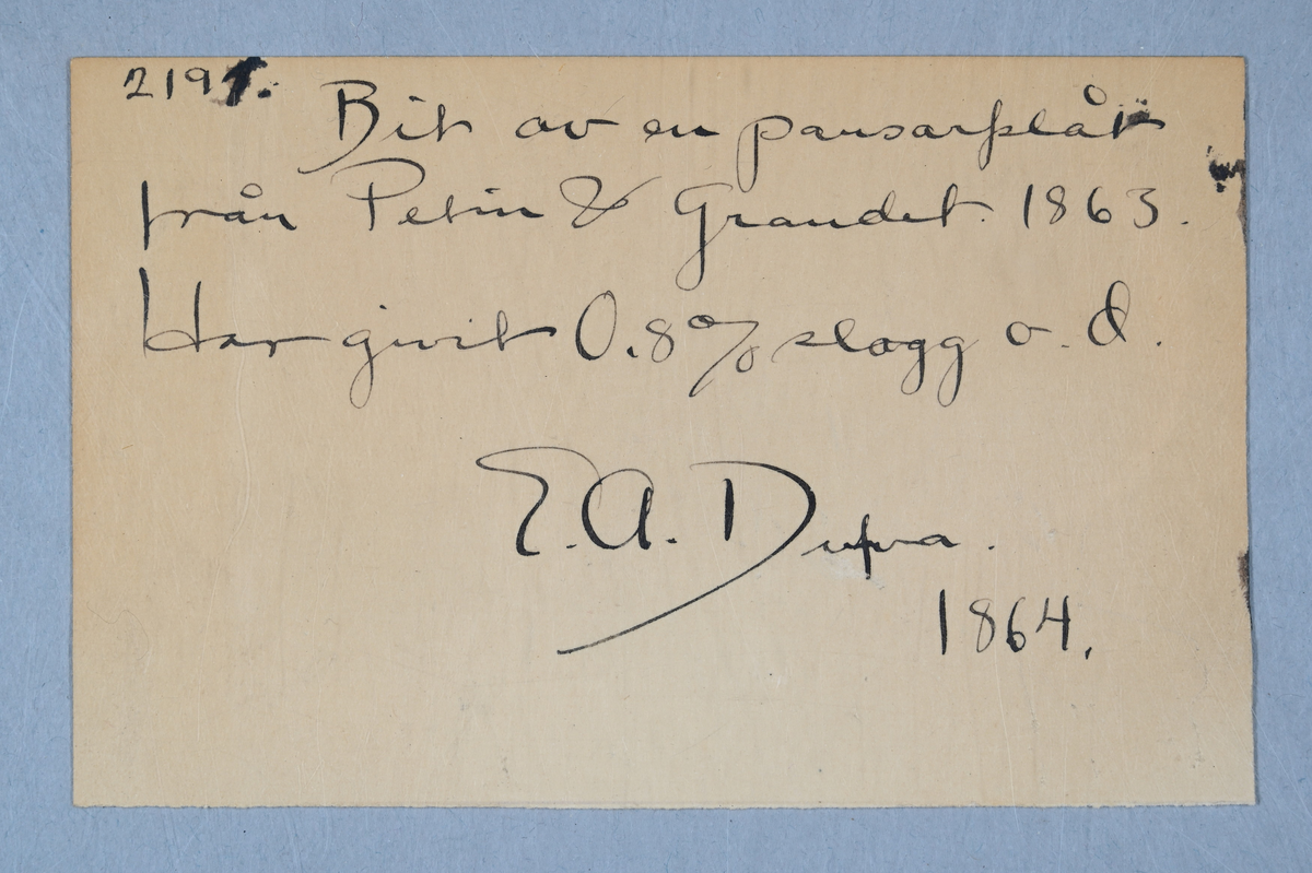 Prov på pansarplåt. Märkning på provet med påklistrad lapp med notering: "Gauder & Petin (?) pantzarplåt, 1863." Två tillhörande lappar med notering: "2119. Bit av pansarplåt från Petin & Grandet år 1863. Har givit 0,8% slagg o.d. E. A. Dufva. 1864."
