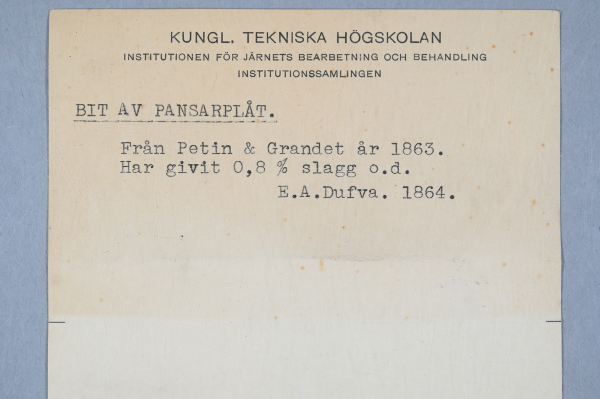 Prov på pansarplåt. Märkning på provet med påklistrad lapp med notering: "Gauder & Petin (?) pantzarplåt, 1863." Två tillhörande lappar med notering: "2119. Bit av pansarplåt från Petin & Grandet år 1863. Har givit 0,8% slagg o.d. E. A. Dufva. 1864."