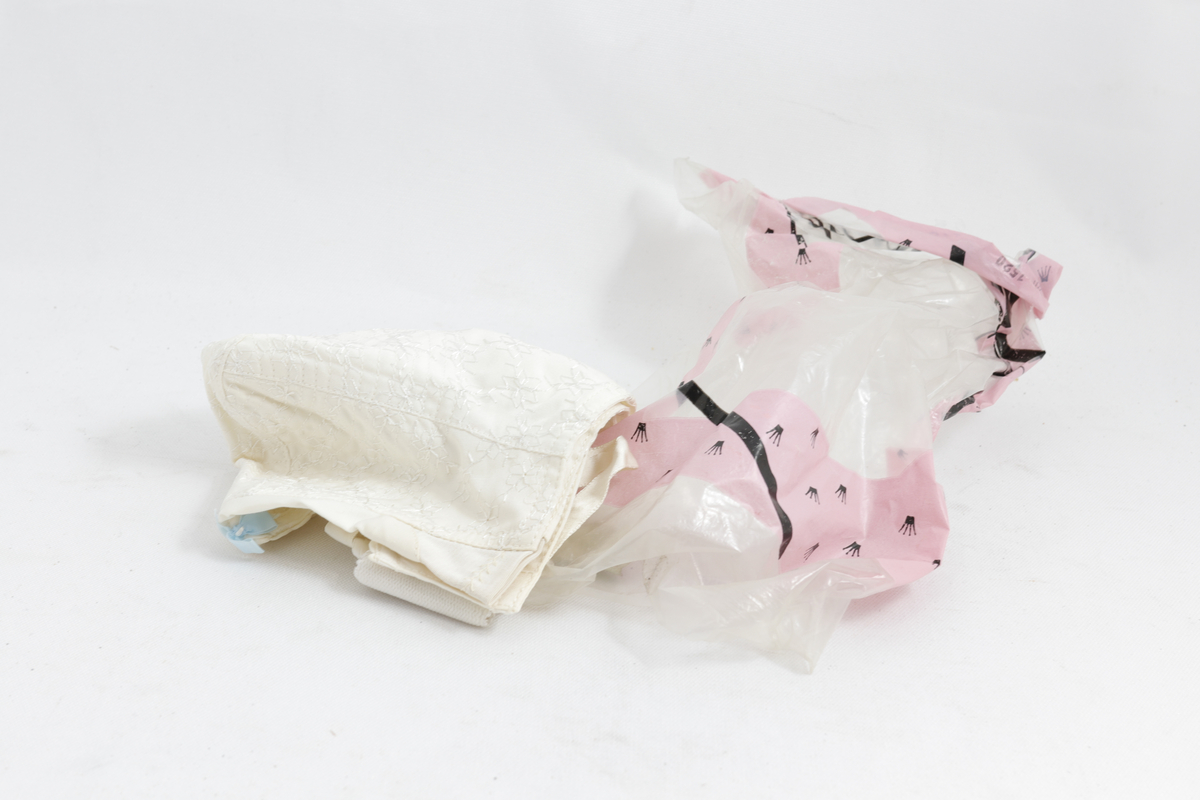Brystholder i gjennomsiktig og rosa plastpose. Brystholderen er hvit med blonder og en blå sløyfe.