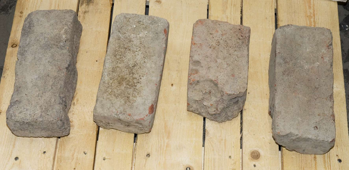 Fyra stycken tegelstenar med rester efter murbruk. En sten har avtryck efter fingrar eller tassavtryck.