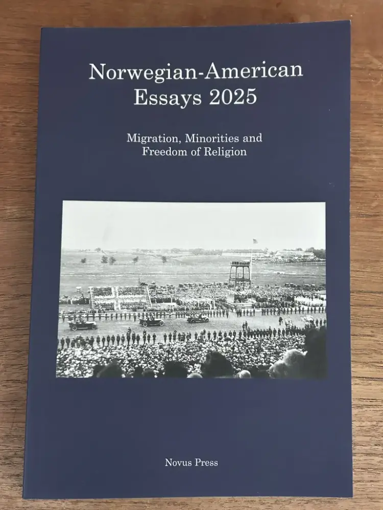 Forside av tidsskriftet Norwegian-American Essays 2025. Mørkeblå bakgrunn og historisk foto av mange publikummere som ser på bilkortesje.