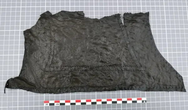 Stort, uregelmessig lærstykke med sømmer, lagt flatt på rutenett med målestokk.