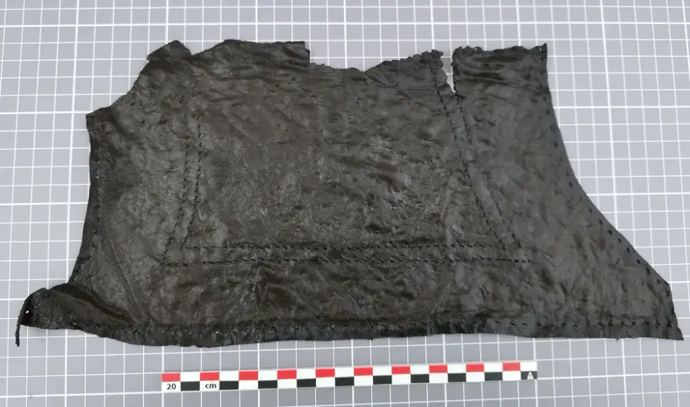 Stort, uregelmessig lærstykke med sømmer, lagt flatt på rutenett med målestokk.