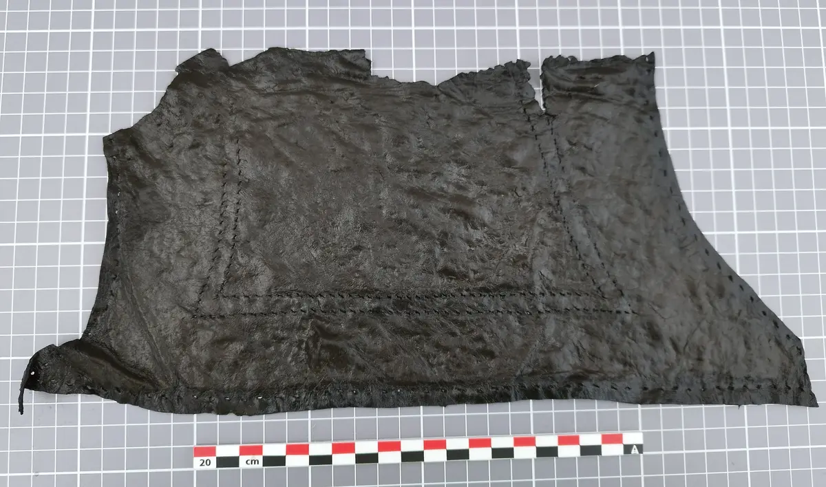 Stort, uregelmessig lærstykke med sømmer, lagt flatt på rutenett med målestokk.