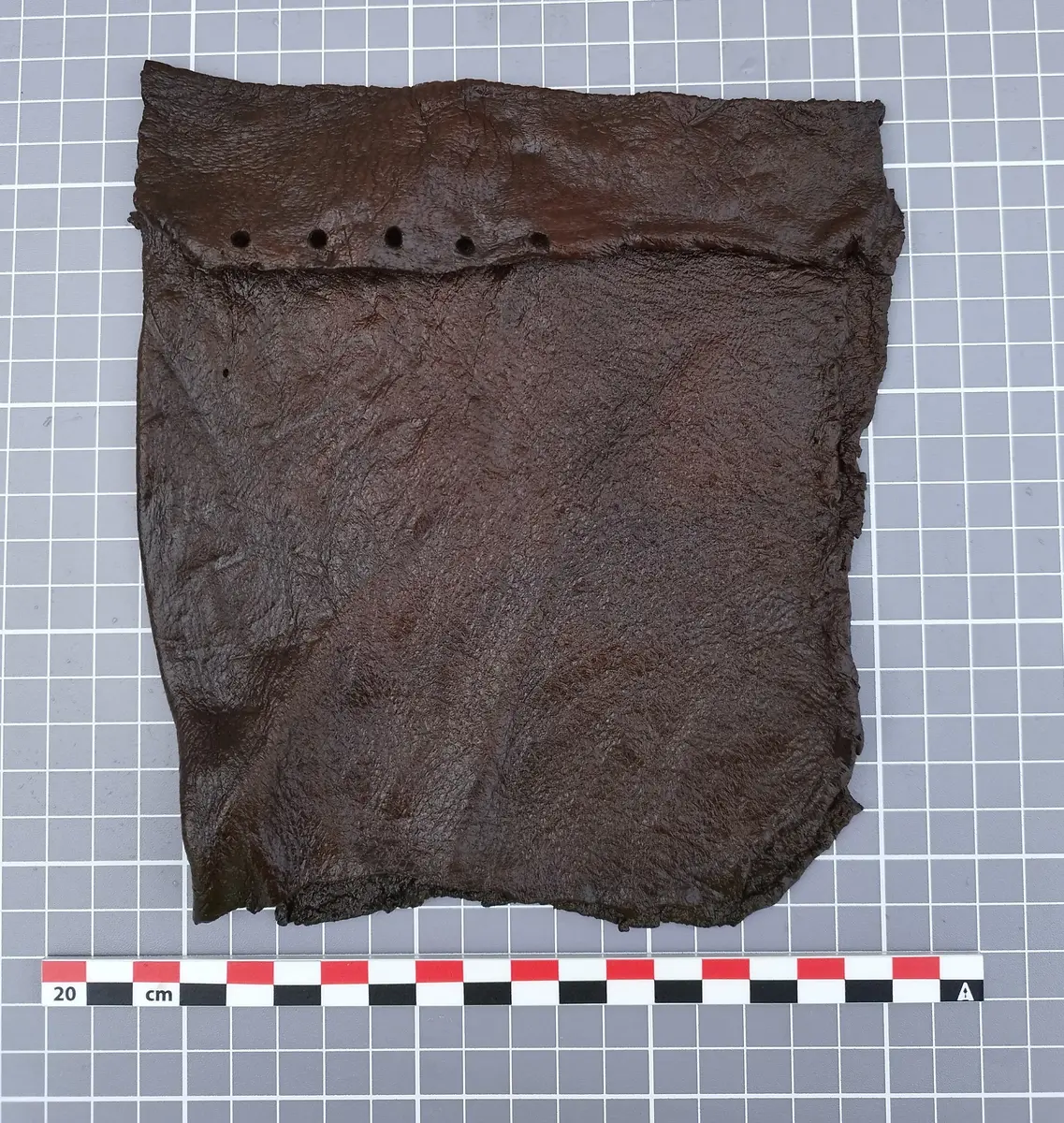 Rektangulært lærstykke med hull langs toppen, funnet under utgravning i Oslo.