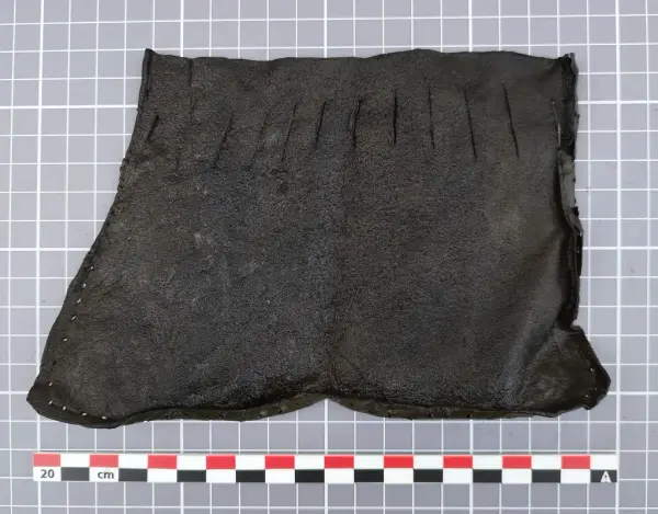 Lærstykke fra middelalderen med jevnt fordelte snitt langs toppen, trolig del av en veske med snøring.