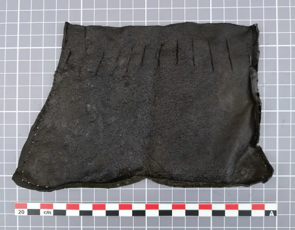 Lærstykke fra middelalderen med jevnt fordelte snitt langs toppen, trolig del av en veske med snøring.