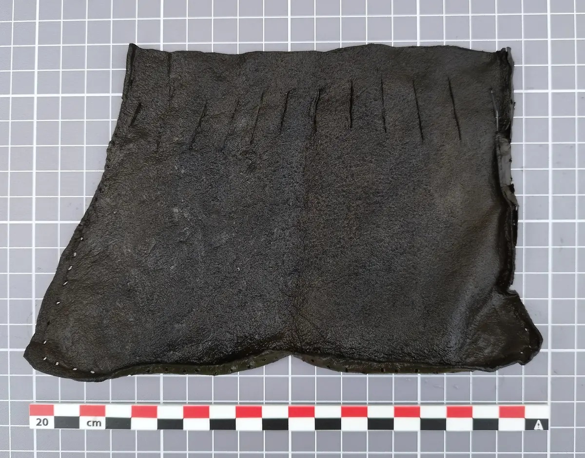 Lærstykke fra middelalderen med jevnt fordelte snitt langs toppen, trolig del av en veske med snøring.