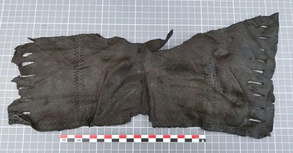  Stykke lær med sømmer og snitt for snøring, trolig del av en middelalderveske.