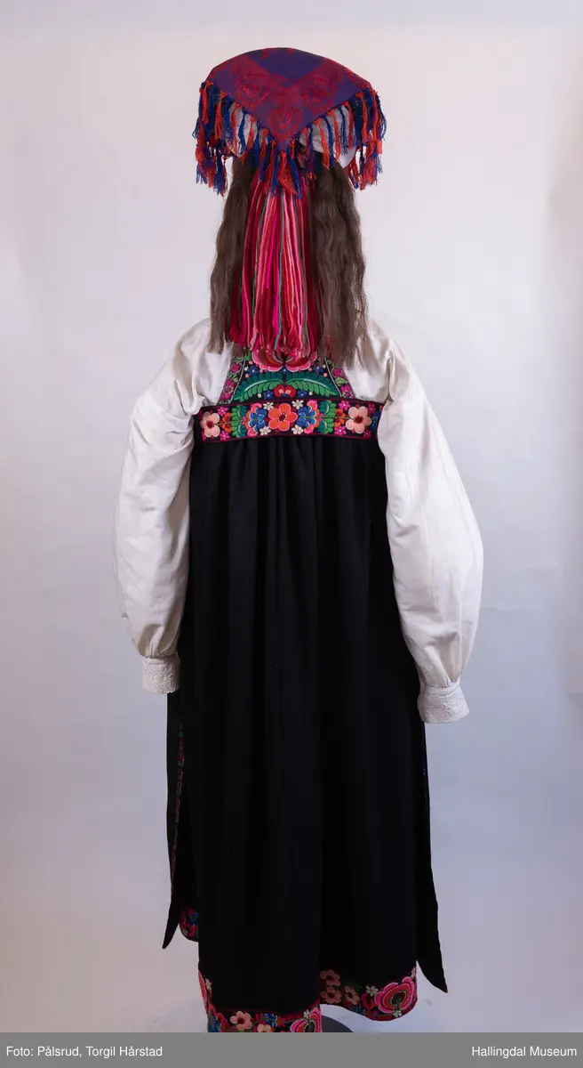 Kone frå Øvre Hallingdal, kyrkjekledd. Viser korleis gifte kvinner kunne gå kledd i Øvre Hallingdal. 

Truleg frå tidleg 1900-tal. Døs i svart ull, med brodert overliv i plattsaum og plattsaumbroderi nedst. forkle i svart ulldamask med plattsaumbroderi nedst. Døsa og forkle er truleg sauma av Birgit Anfinset (f. 1863). Sauma band kom nedanfrå dalen sist på 1800-talet, fyrst som forkleband. Banda var breiast rundt 1920, og denne stakken er truleg frå denne tida.

Hovudbunaden kallast hettepannelin eller lykkjeplagg (Ål), og er hovudbunaden til gifte. Her har silkeplagget (hettepannelinet) vorte stort og ferdigsydd. Storleiken på hettepannelinet har variert frå tid til anna.

Kona står utstilt i den faste bunadsutstillinga på Hol Bygdemuseum. 