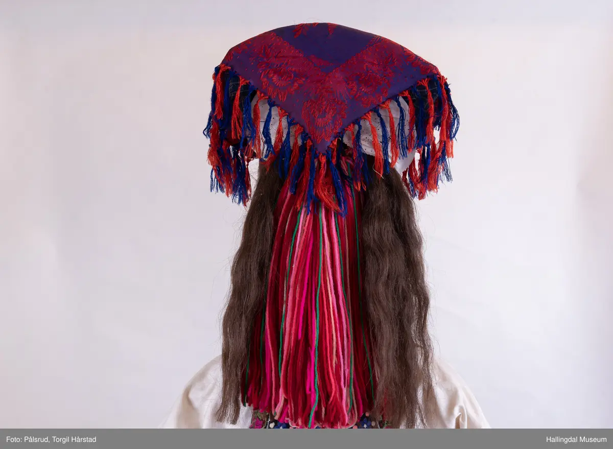 Kone frå Øvre Hallingdal, kyrkjekledd. Viser korleis gifte kvinner kunne gå kledd i Øvre Hallingdal. 

Truleg frå tidleg 1900-tal. Døs i svart ull, med brodert overliv i plattsaum og plattsaumbroderi nedst. forkle i svart ulldamask med plattsaumbroderi nedst. Døsa og forkle er truleg sauma av Birgit Anfinset (f. 1863). Sauma band kom nedanfrå dalen sist på 1800-talet, fyrst som forkleband. Banda var breiast rundt 1920, og denne stakken er truleg frå denne tida.

Hovudbunaden kallast hettepannelin eller lykkjeplagg (Ål), og er hovudbunaden til gifte. Her har silkeplagget (hettepannelinet) vorte stort og ferdigsydd. Storleiken på hettepannelinet har variert frå tid til anna.

Kona står utstilt i den faste bunadsutstillinga på Hol Bygdemuseum. 