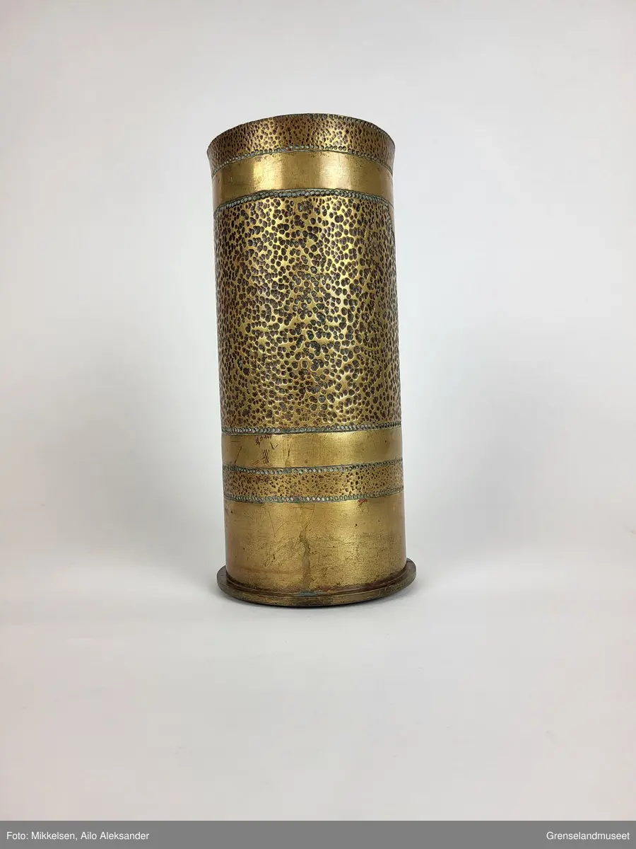 En (antagelig) norsk soldat som står og speider fra toppen av en knaus eller en høyde. Et maskingevær står på en tripod ved føttene til soldaten i profil. Motivet er innrisset for hånd, trolig med stein eller en form for metall redskap.