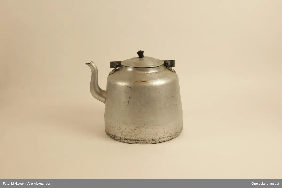 Gjenstanden er stor kaffekjele i jern, med original lokk og hanke medbrakt. Kaffekjelens innside viser at den har vært godt brukt med brunsvidde flekker fra kaffekoking. Utsiden er er jern grå, men undersiden har lag med svart svidd sot og rester. Det er en liten ripe på kjelens venstre side når man holder den i handtak. Ripen er ikke stor eller omfattende, men har fått litt rust som dekker det eksponerte underlaget av jern. Handtaket er jerngrått som resten av gjenstanden, men har med tiden fått et brunt fargeskjær på seg.         
