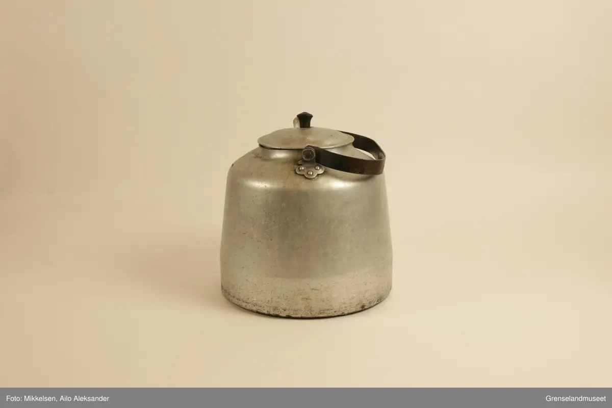 Gjenstanden er stor kaffekjele i jern, med original lokk og hanke medbrakt. Kaffekjelens innside viser at den har vært godt brukt med brunsvidde flekker fra kaffekoking. Utsiden er er jern grå, men undersiden har lag med svart svidd sot og rester. Det er en liten ripe på kjelens venstre side når man holder den i handtak. Ripen er ikke stor eller omfattende, men har fått litt rust som dekker det eksponerte underlaget av jern. Handtaket er jerngrått som resten av gjenstanden, men har med tiden fått et brunt fargeskjær på seg.         