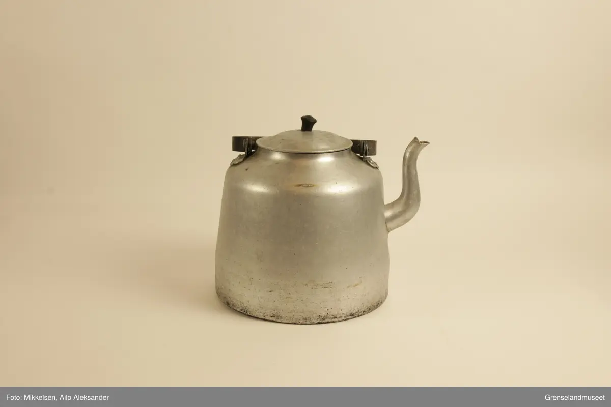 Gjenstanden er stor kaffekjele i jern, med original lokk og hanke medbrakt. Kaffekjelens innside viser at den har vært godt brukt med brunsvidde flekker fra kaffekoking. Utsiden er er jern grå, men undersiden har lag med svart svidd sot og rester. Det er en liten ripe på kjelens venstre side når man holder den i handtak. Ripen er ikke stor eller omfattende, men har fått litt rust som dekker det eksponerte underlaget av jern. Handtaket er jerngrått som resten av gjenstanden, men har med tiden fått et brunt fargeskjær på seg.         