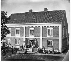 Hovedbygningen på øvre Hammerstad i Totenvika en gang før 1900. I dæråpningen står Marie Pedersdtr., født Hveem, og hennes mann gårdbruker Ole Jensen Hammerstad. Ingen av de øvrige personene er identifisert.