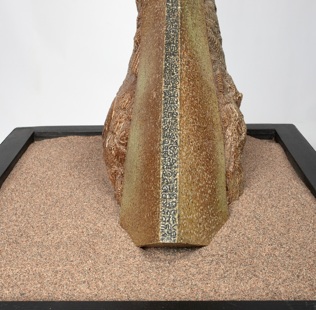 Keramisk skulptur på sort sokkel med sand. Skulpturen består av organiske former som stiger opp av sanda. I formene er det avtrykk som forestiller fossiler, avtrykk av bein og abstrakte former. Skulpturen er glasert beige og brun.