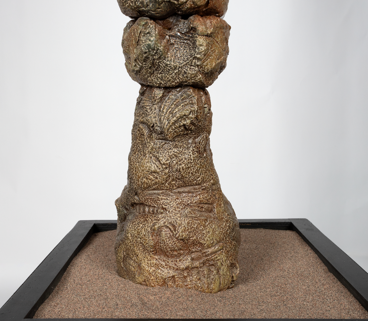 Keramisk skulptur på sort sokkel med sand. Skulpturen består av organiske former som stiger opp av sanda. I formene er det avtrykk som forestiller fossiler, avtrykk av bein og abstrakte former. Skulpturen er glasert beige og brun.