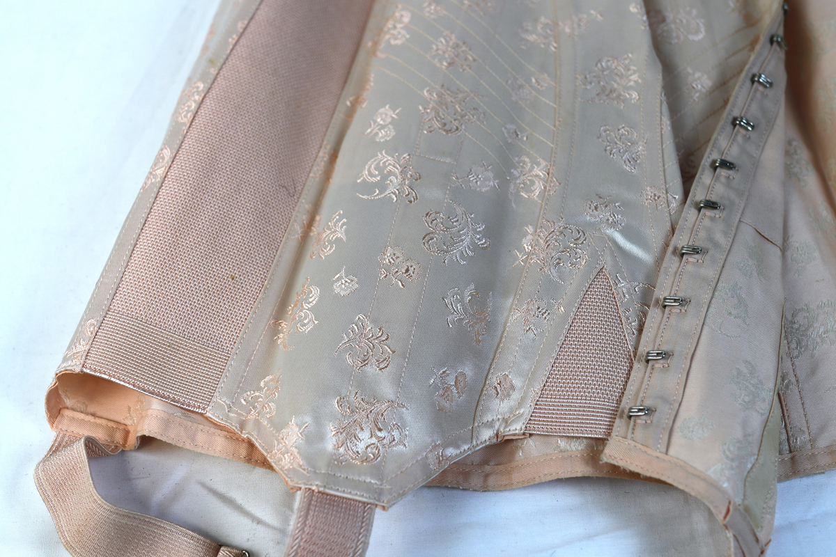 Hofteholder i rosa med brodert mønster.