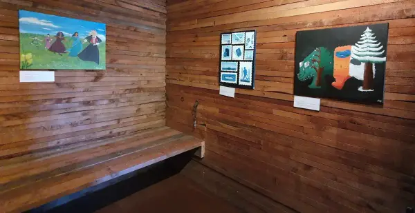 Tre maleri utstilt på bare trevegger i fengselet. Det ene viser kvinner i ulike nasjonaldrakter, ett viser frimerker, ett viser en bjørn med fargerik drakt som representerer årstidene