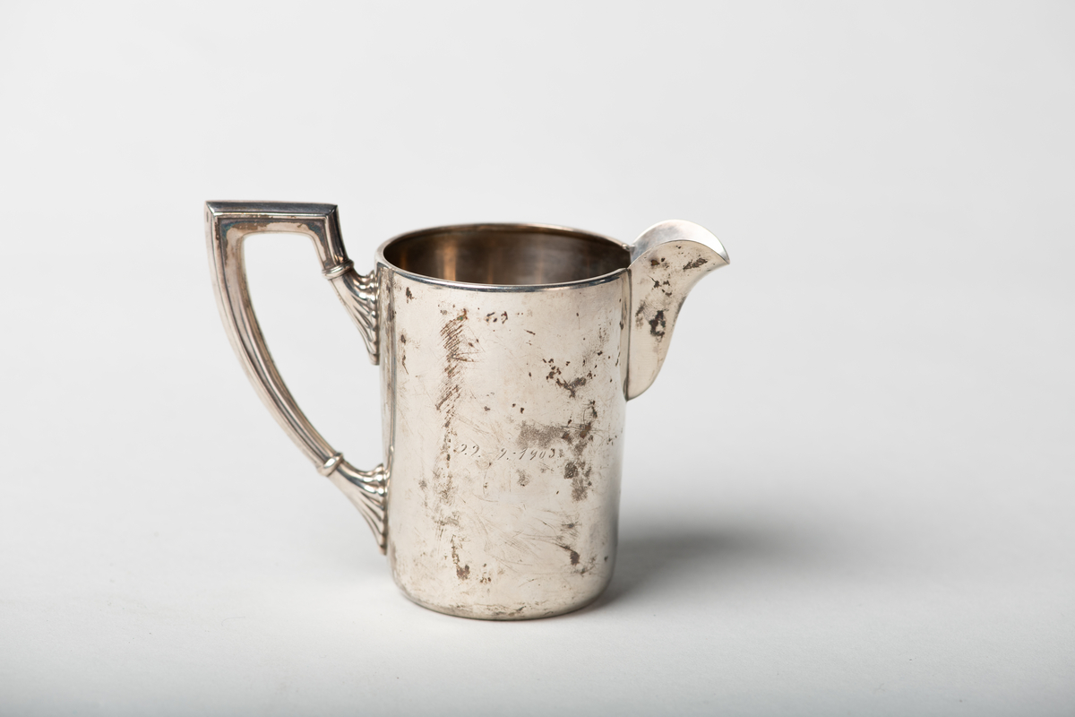 Sukkerkopp i begerform med inngravert monogram. Fløtemugge med riflet og knekket hank, korpus sylinderformet med bred tut. Monogram H F.