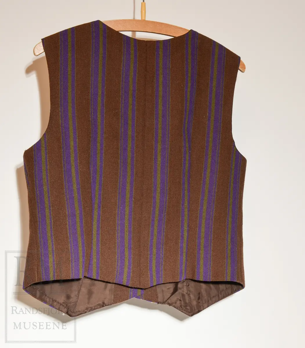 a. Cape med krage og stofftrukne knapper, foret med lilla kunstsilke. b. Vest i stripete stoff, samme fargekombinasjon som det rutete. Stofftrukne knapper og brunt silkefor. c. Omslagsskjørt i rutete ullstoff med plisseringer/folder. Lukning foran på siden (stoftrukne knapper, spenne i linningen) Foret med brunt silkestoff (samme som vest, kunstsilke).
Renneliste (tråder)
36 brun
2 grønn
4 lilla
2 grønn
12 lilla
8 grønn
8 lilla
2 grønn