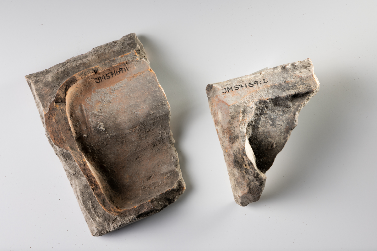 Kakel, två fragment, av lertegel, profilerat med vit glasyr med blå stänk.

JM.57169:1 Profilerat kakelkrön
JM.57169: 2 Böjd kakelbit med profilerad kant