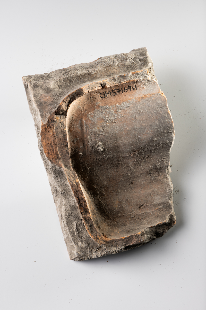 Kakel, två fragment, av lertegel, profilerat med vit glasyr med blå stänk.

JM.57169:1 Profilerat kakelkrön
JM.57169: 2 Böjd kakelbit med profilerad kant