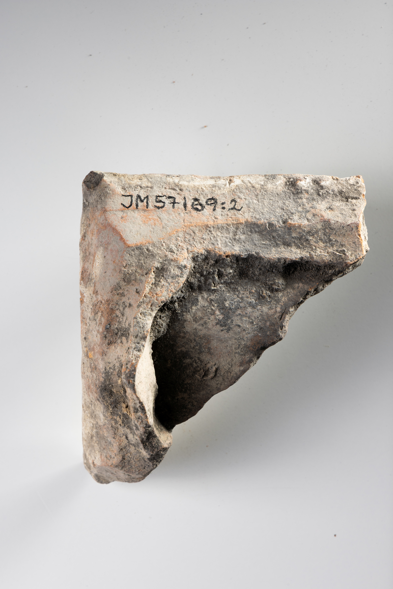 Kakel, två fragment, av lertegel, profilerat med vit glasyr med blå stänk.

JM.57169:1 Profilerat kakelkrön
JM.57169: 2 Böjd kakelbit med profilerad kant