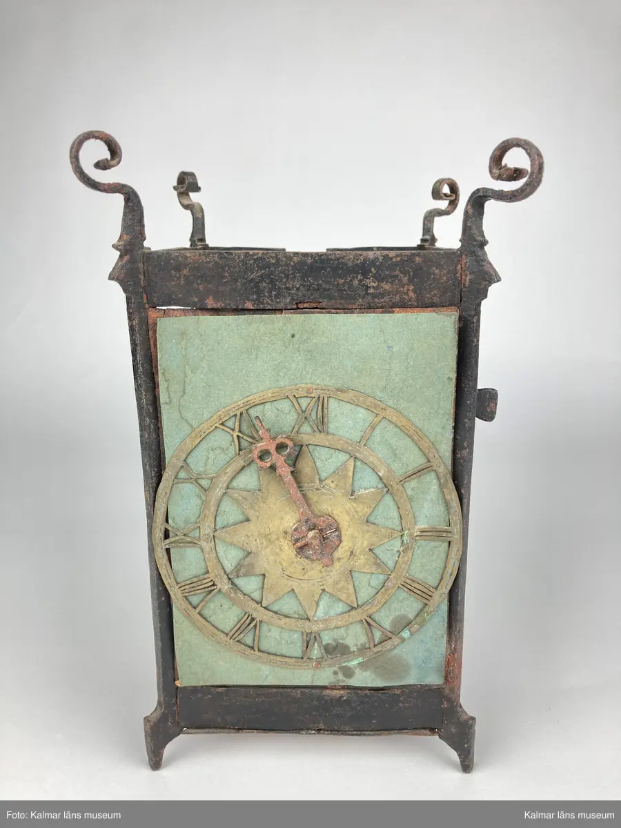 KLM 46893. Bordsur. Rektangulär stomme av järn med öppningsbara sidor, varav ena sidans dörr saknas. Upptill smidda detaljer. På ena sidan urtavla av mässing med stjärna i mitten, en visare av järn. Bakom urtavlan ett blekt pappersark i blågrönt. Urverk av järn och mässing. Uret har fyra fötter. På baksidan ögla av järn. Pendel, lodlinor, lod och trissor saknas.