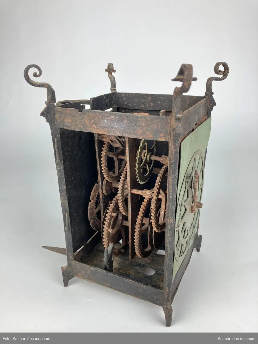 KLM 46893. Bordsur. Rektangulär stomme av järn med öppningsbara sidor, varav ena sidans dörr saknas. Upptill smidda detaljer. På ena sidan urtavla av mässing med stjärna i mitten, en visare av järn. Bakom urtavlan ett blekt pappersark i blågrönt. Urverk av järn och mässing. Uret har fyra fötter. På baksidan ögla av järn. Pendel, lodlinor, lod och trissor saknas.