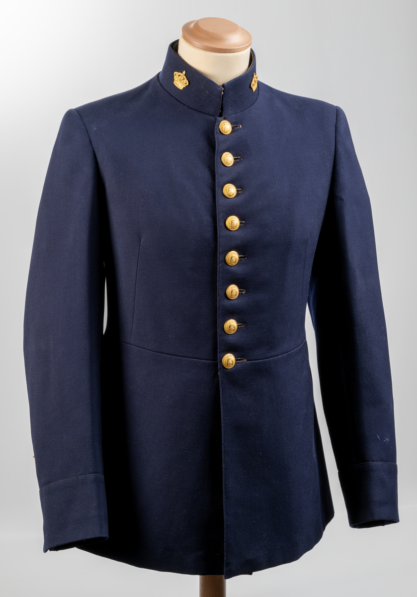 Uniformsjacka. Mörkblå. Enkel knäppning framtill med åtta knappar. På nedre delen av ärmarna tre mindre knappar. Sprund baktill med sex knappar. Alla uniformsknappar förgyllda och präglade med Växjö stadsvapen (år 1926-39). Kragmärke på var sida av ståndkragen, en förgylld kunglig krona med kudde.