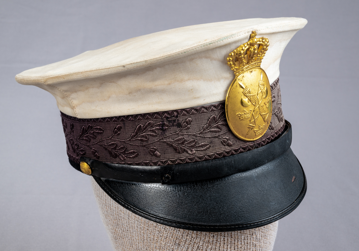 Skärmmössa till sommaruniform. Vitt kläde, platt kulle med mönstervävt mössband med eklövsmotiv. Svettrem i brunt läder. Svart skärm i läder. Svart hakband som är fäst med två mindre förgyllda knappar, präglade med Växjö stadsvapen (år 1926-39). Mössmärke för konstapel, förgylld oval sköld med korslagda fasces (spöknippe), lilla riksvapnet (tre kronor) krönt med kunglig krona med kudde.