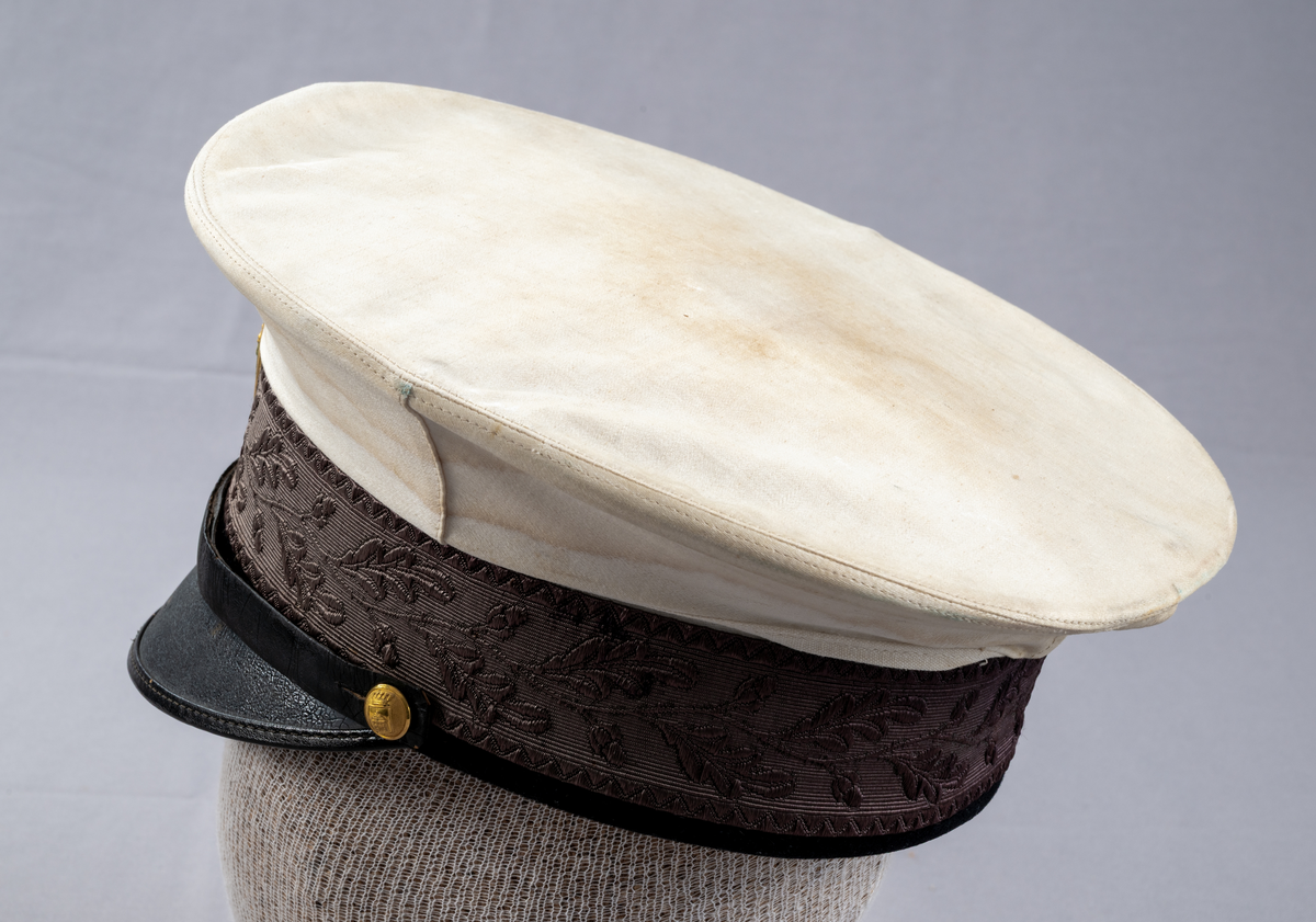Skärmmössa till sommaruniform. Vitt kläde, platt kulle med mönstervävt mössband med eklövsmotiv. Svettrem i brunt läder. Svart skärm i läder. Svart hakband som är fäst med två mindre förgyllda knappar, präglade med Växjö stadsvapen (år 1926-39). Mössmärke för konstapel, förgylld oval sköld med korslagda fasces (spöknippe), lilla riksvapnet (tre kronor) krönt med kunglig krona med kudde.