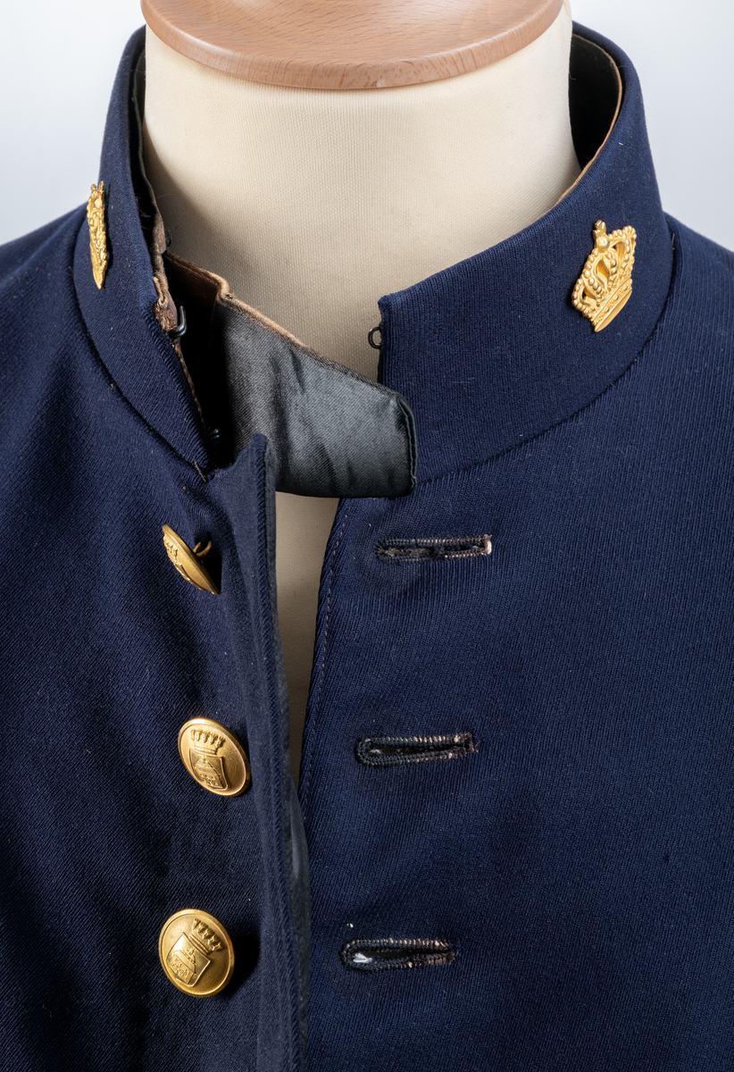 Uniformsjacka. Mörkblå. Enkel knäppning framtill med åtta knappar. På nedre delen av ärmarna tre mindre knappar. Sprund baktill med sex knappar. Alla uniformsknappar förgyllda och präglade med Växjö stadsvapen (år 1926-39). Kragmärke på var sida av ståndkragen, en förgylld kunglig krona med kudde.