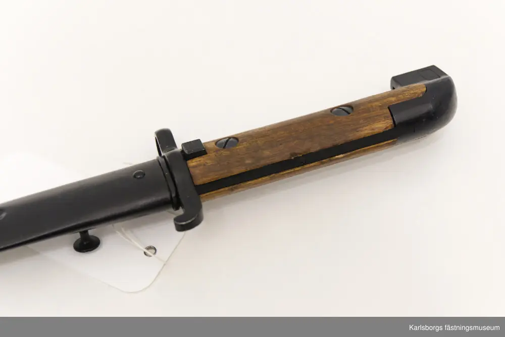 Bajonett m/1914, för karbin m/1894-1914. Bajonett är ett blankvapen som fästs vid mynningen på musköter, gevär eller karbiner och som används i närstrid. Karbin m/1894-1914 saknade ursprungligen bajonett, men försågs år 1914 med sådan. Märkt EJ AB (Eskilstuna Jernmanufaktur AB). Bajonetten kommer med bajonettbalja. Handtag av metall och trä.