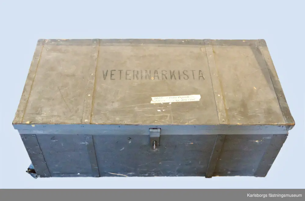 Kista med veterinärutrustning för häst, uppskattad från 1960-1970-talen. Veterinärkistan innehåller bandage och gips, borstar, instrument, ljus, tändstickor, termometrar, säkerhetsnålar, två stycken handdukar, två stycken kanyler, två stycken skedar, tvålar, bomull, trattar, portfölj med anteckningsblock, anteckningshäften mm. Ett verktyg som tycks ha tillkommit till kistan på senare tid är en äldre tysk militärficklampa, Daimon Telko, uppskattat från 1930-1940-talen. En del av utrustningen fattas, bland annat gummihandskar, elastiskt bandage för hästens ben, rekondspruta 10ml, bägare i emalj 100ml och ljusstake. Vissa sprickor finns i botten. Veterinärkistan togs ut på fält ihop med militären och deras hästar.