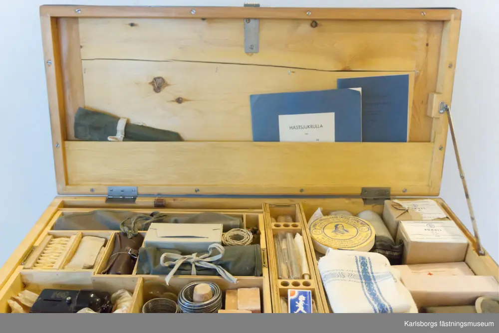 Kista med veterinärutrustning för häst, uppskattad från 1960-1970-talen. Veterinärkistan innehåller bandage och gips, borstar, instrument, ljus, tändstickor, termometrar, säkerhetsnålar, två stycken handdukar, två stycken kanyler, två stycken skedar, tvålar, bomull, trattar, portfölj med anteckningsblock, anteckningshäften mm. Ett verktyg som tycks ha tillkommit till kistan på senare tid är en äldre tysk militärficklampa, Daimon Telko, uppskattat från 1930-1940-talen. En del av utrustningen fattas, bland annat gummihandskar, elastiskt bandage för hästens ben, rekondspruta 10ml, bägare i emalj 100ml och ljusstake. Vissa sprickor finns i botten. Veterinärkistan togs ut på fält ihop med militären och deras hästar.