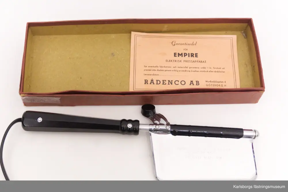 Empire Elektrisk Pressapparat från 1950-talet. Används för pressveck på plagg: byxor, kjolar, rockar, slipsar mm. Den kunde användas direkt på plagget och sägs ha skapat pressveck som kunde vara i flera veckor. Användningen gick till såhär: först fick pressapparaten värmas upp i ungefär tre minuter för att sedan föra den sakta efter vecket så att den glider fint. Plagget skulle inte sträckas ut under arbetet. Pressen kunde inte överhettas och heller inte skada plagget. En garantisedel medföljer men leveransdatum saknas. Föremålet förvaras i sammanhörande låda. Tillverkat i Storbritannien. 
