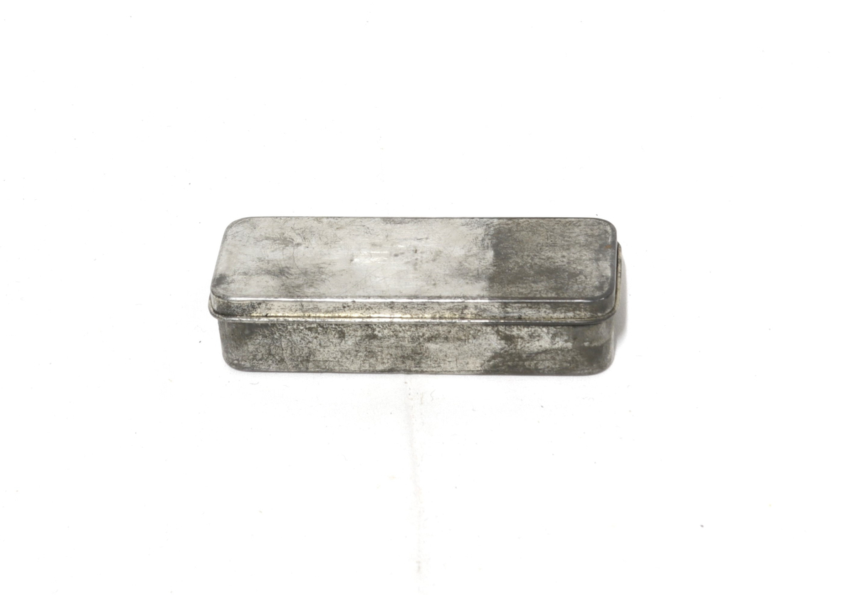 Rektangulær boks med hengslet lokk, inni ligger 6 løse deler:
2 fjærer, 1 sylinder, 2 nettinger, 1 liten metalldel.
Tilhører et sett med utstyr for rengjøring og istandsetting av våpen.