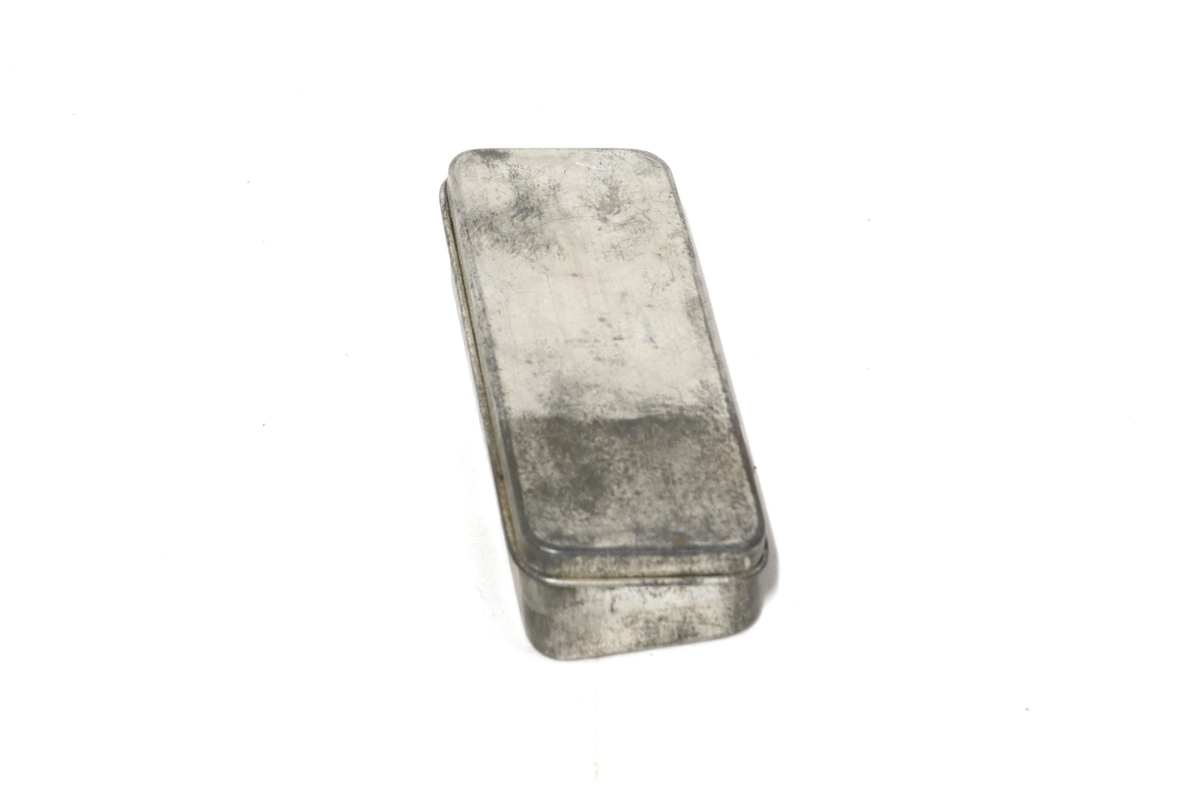 Rektangulær boks med hengslet lokk, inni ligger 6 løse deler:
2 fjærer, 1 sylinder, 2 nettinger, 1 liten metalldel.
Tilhører et sett med utstyr for rengjøring og istandsetting av våpen.