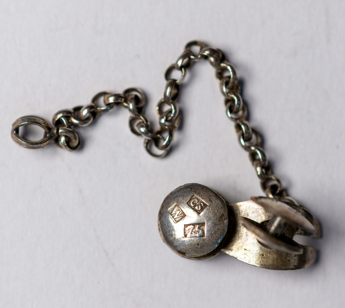 Kedja, fäst vid en stolpknapp. En stolpknapp rörlig längs kedjan. Silver .Längd 7,5 cm. (kedja)Diameter 0,8 cm (knappar)Stämplar: se bildZ5=1878