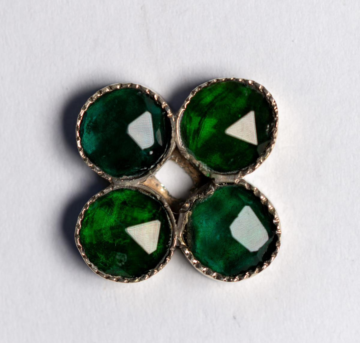 Brudkrona av silverplåt. Oval rak sida av 7 hoplödda plåtar som upptill svänger ut och avslutas i treflikade krön. Buckelornamentik samt svisselerade mönster. Fyrpassformade infattningar av röda och gröna glasstenar på varje flik. Ytterligare dekorerad med påsatta löst hängande förgyllda löv samt halvsfäriska hängen. Kronan avslutas nertill med en påsatt vulst. Stämplar: 13 1/3 (lödighet), LMS (=LM Salvesen), (Ålesunds stadsvapen), 1854.Mått upptill: längd 23 cm, bredd 23 cm.nertill: längd 17 cm, bredd 16 cm, höjd 17 cm.