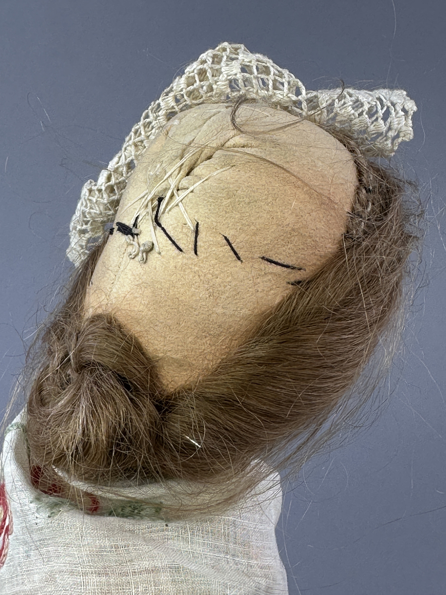 Docka klädd i kvinnlig sockendräkt föreställande Jösse härad i Värmland (hätta från Brunskog). Huvud och händer sydda av sämskskinn samt kropp av satin-tyg.