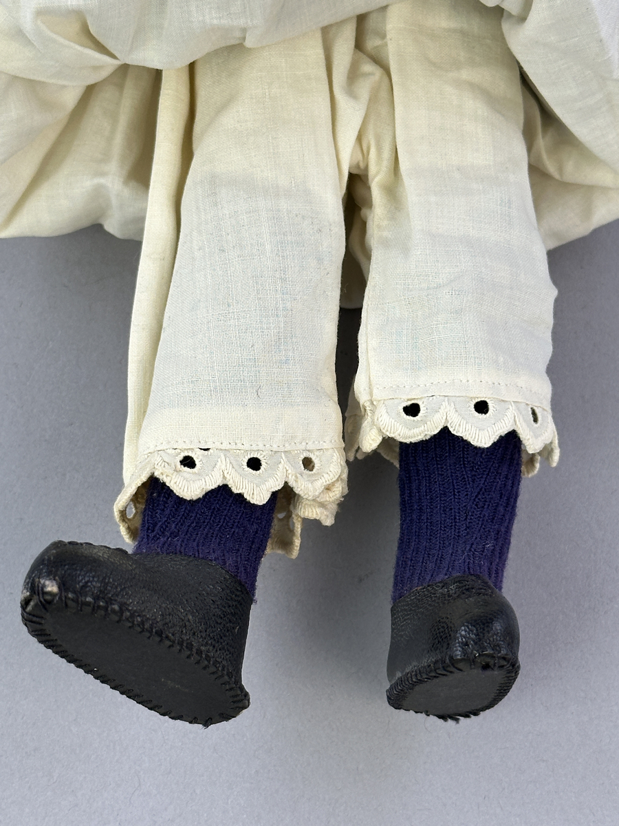 Docka klädd i kvinnlig sockendräkt föreställande Jösse härad i Värmland (hätta från Brunskog). Huvud och händer sydda av sämskskinn samt kropp av satin-tyg.