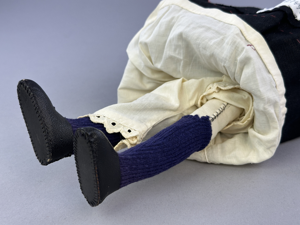 Docka klädd i kvinnlig sockendräkt föreställande Jösse härad i Värmland (hätta från Brunskog). Huvud och händer sydda av sämskskinn samt kropp av satin-tyg.