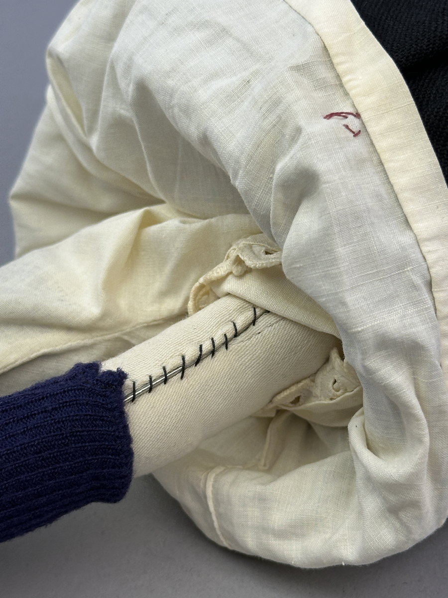 Docka klädd i kvinnlig sockendräkt föreställande Jösse härad i Värmland (hätta från Brunskog). Huvud och händer sydda av sämskskinn samt kropp av satin-tyg.